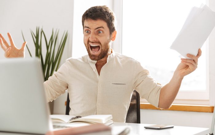 Un homme agressif face à un ordinateur dans un bureau - concept illustrant la difficulté du recouvrement des créances