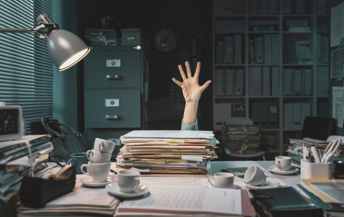 La surchage de travail des entrepreneurs : une main qui dépasse d'un bureau couvert de dossiers